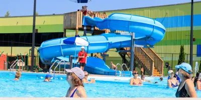 People in swimming pool and kids using spiral slide.